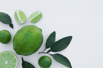 Whole and cut fresh limes with leaves on white background, flat lay. Space for text