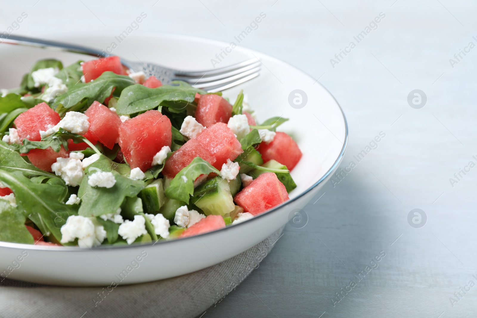 Photo of Delicious salad with watermelon, cucumber, arugula and feta cheese on white table, closeup. Space for text