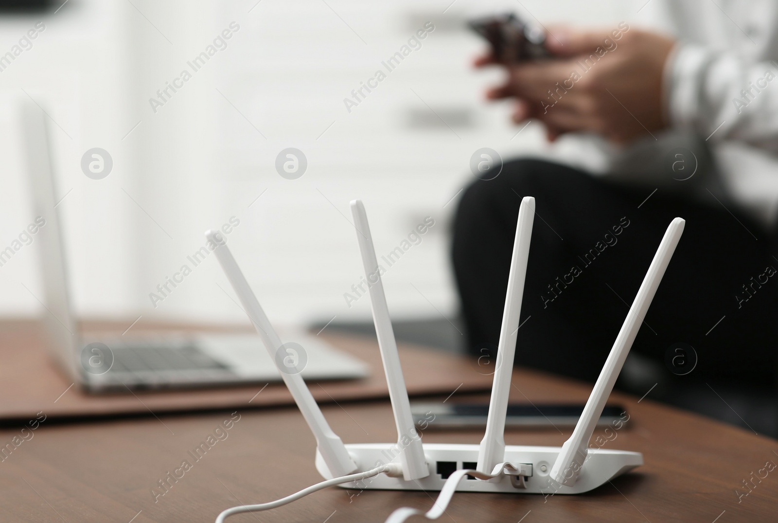 Photo of Man with smartphone and laptop working at wooden table, focus on Wi-Fi router