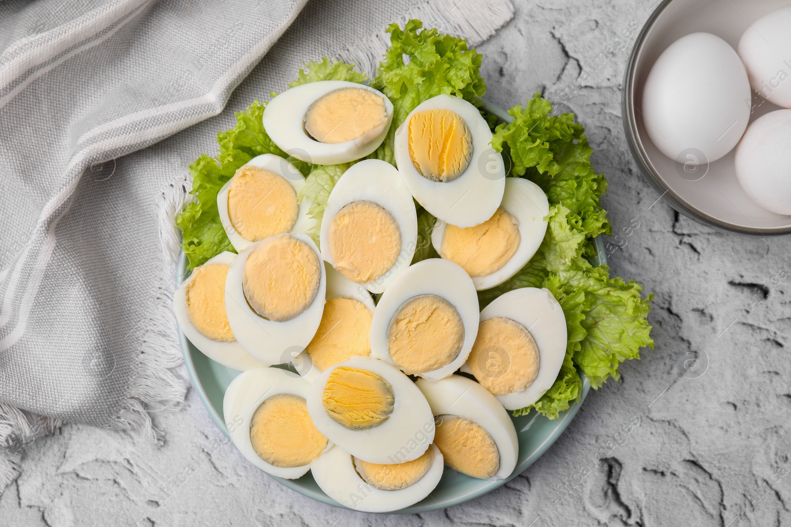 Photo of Fresh hard boiled eggs and lettuce on light grey textured table, top view