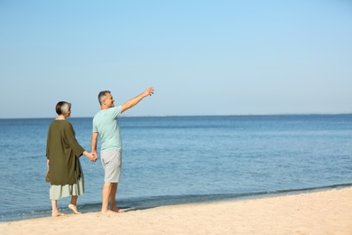 Happy mature couple walking at beach on sunny day