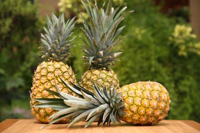 Delicious ripe pineapples on wooden table outdoors, space for text