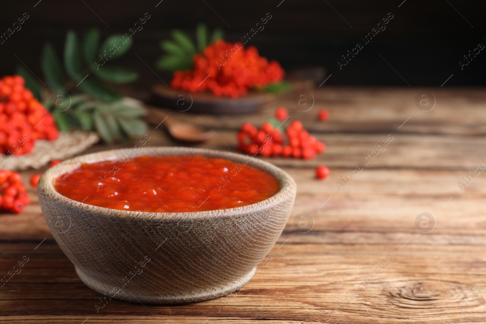 Photo of Delicious rowan jam in bowl on wooden table. Space for text