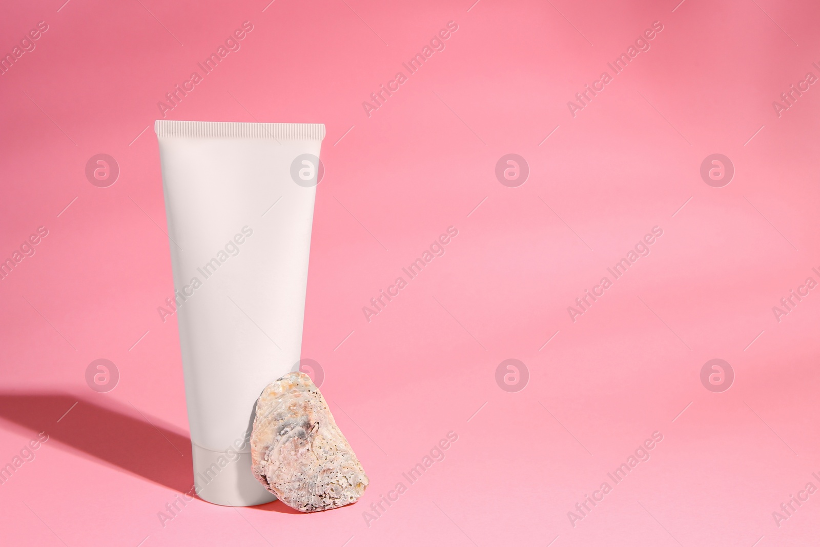 Photo of Tube of cream and stone on pink background. Space for text