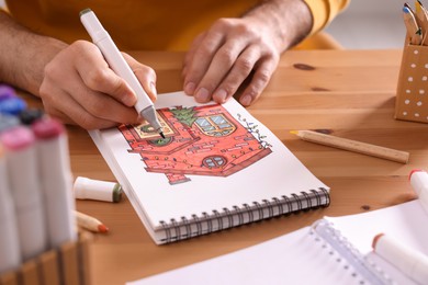 Photo of Man drawing in sketchbook with felt tip pen at wooden table, closeup