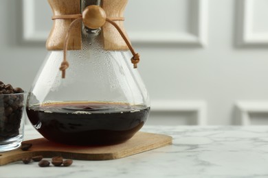 Glass chemex coffeemaker with coffee and beans on white marble table, closeup. Space for text