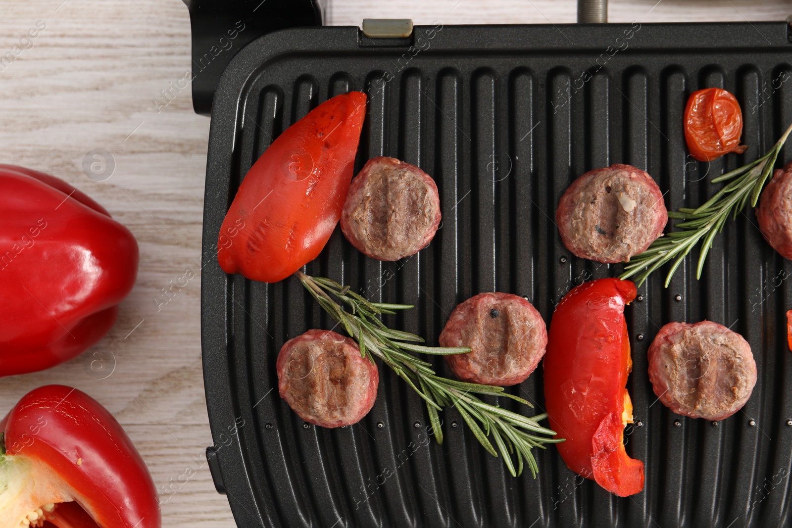 Photo of Electric grill with vegetables, meat balls and rosemary on wooden table, flat lay