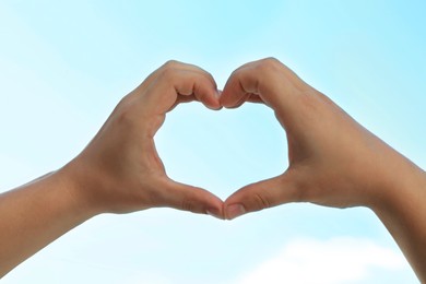 Man making heart with hands outdoors on sunny day, closeup