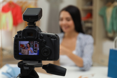 Fashion blogger recording new video at table indoors, focus on camera