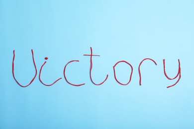 Photo of Word Victory made of threads on color background, top view