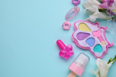 Photo of Decorative cosmetics for kids. Eye shadow palette, lipsticks, accessories and flowers on light blue background, flat lay. Space for text