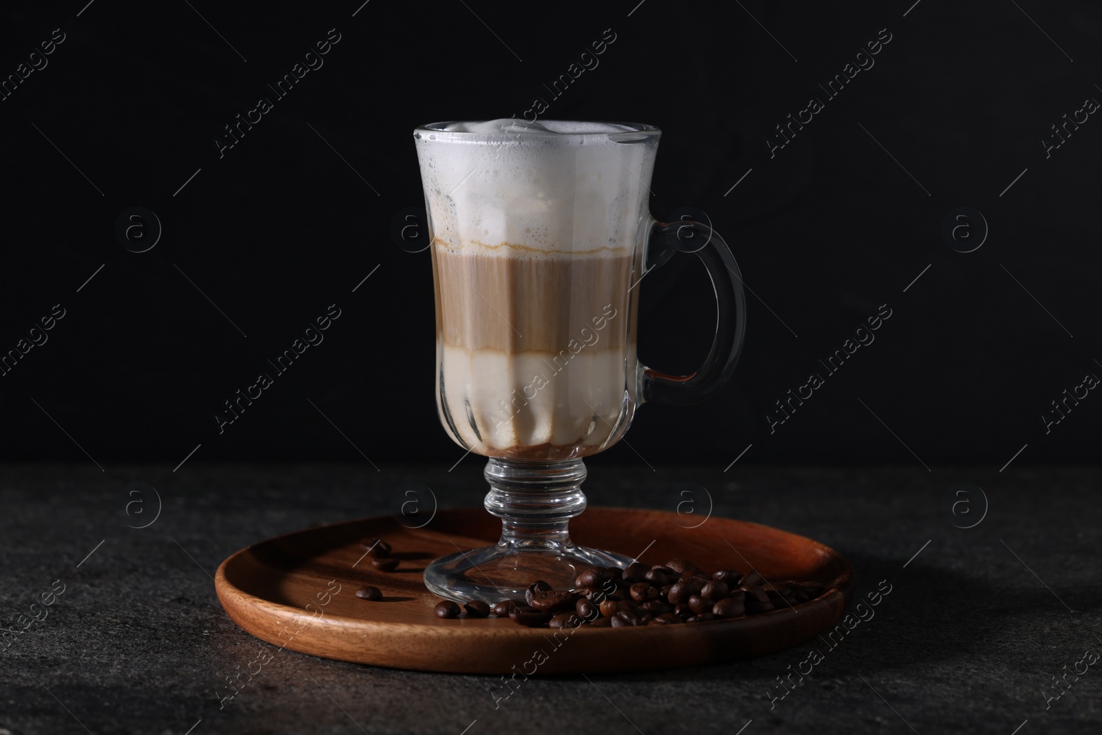 Photo of Aromatic latte macchiato in glass and coffee beans on dark grey table