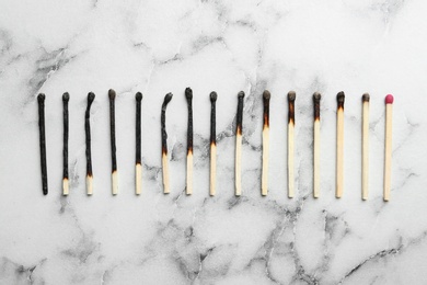 Photo of Row of burnt matches and whole one on marble background, flat lay. Human life phases concept