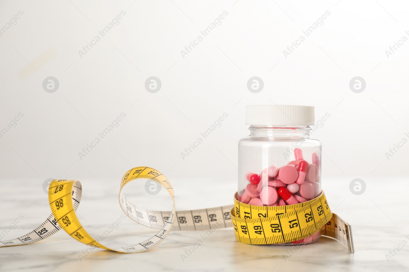 Photo of Jar of weight loss pills and measuring tape on white marble table. Space for text