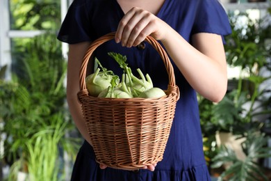 Photo of Woman holding wicker basket with ripe kohlrabi plants outdoors, closeup