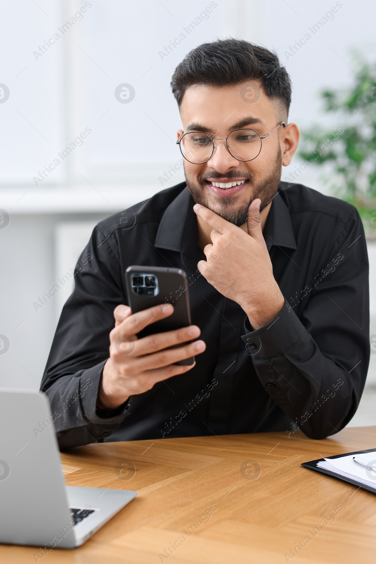 Photo of Handsome young man using smartphone at wooden table in office