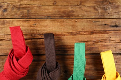 Colorful karate belts on wooden background, flat lay. Space for text