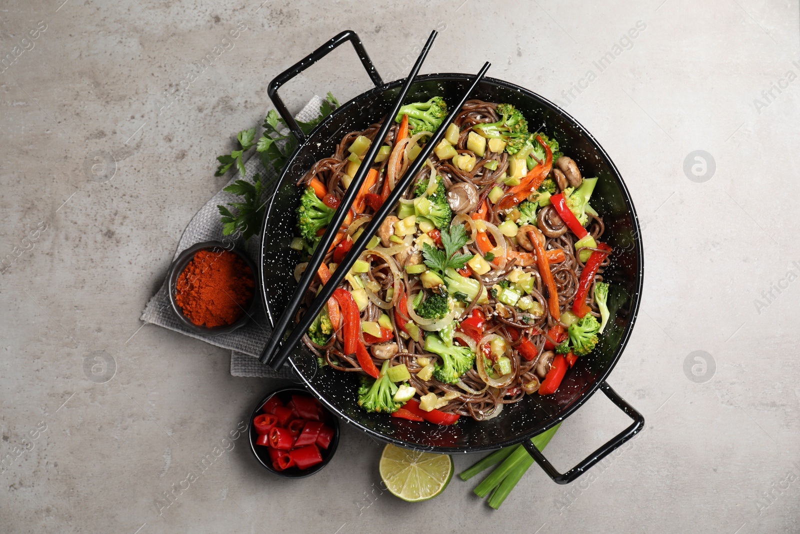 Photo of Stir-fry. Tasty noodles with meat in wok, chopsticks and ingredients on grey textured table, flat lay