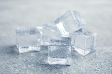 Photo of Ice cubes with water drops on light stone table, closeup