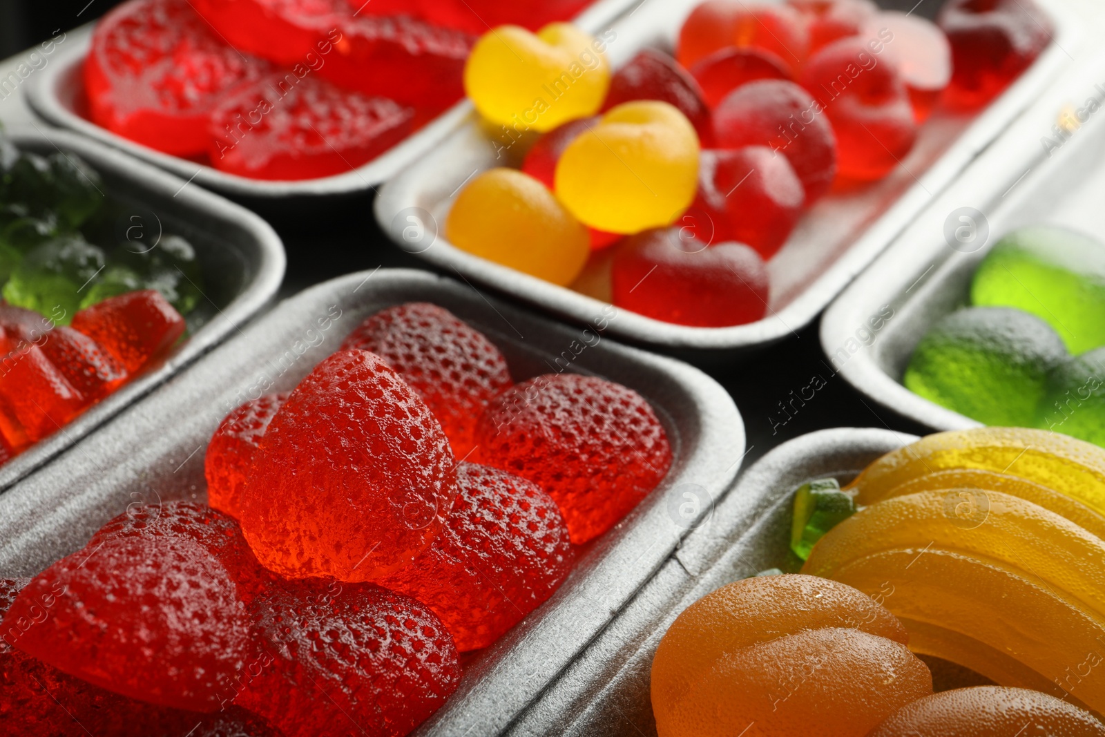 Photo of Different delicious gummy candies in containers, closeup