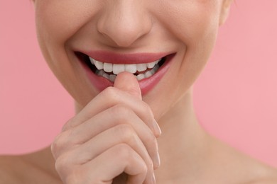 Photo of Young woman biting her finger on pink background, closeup