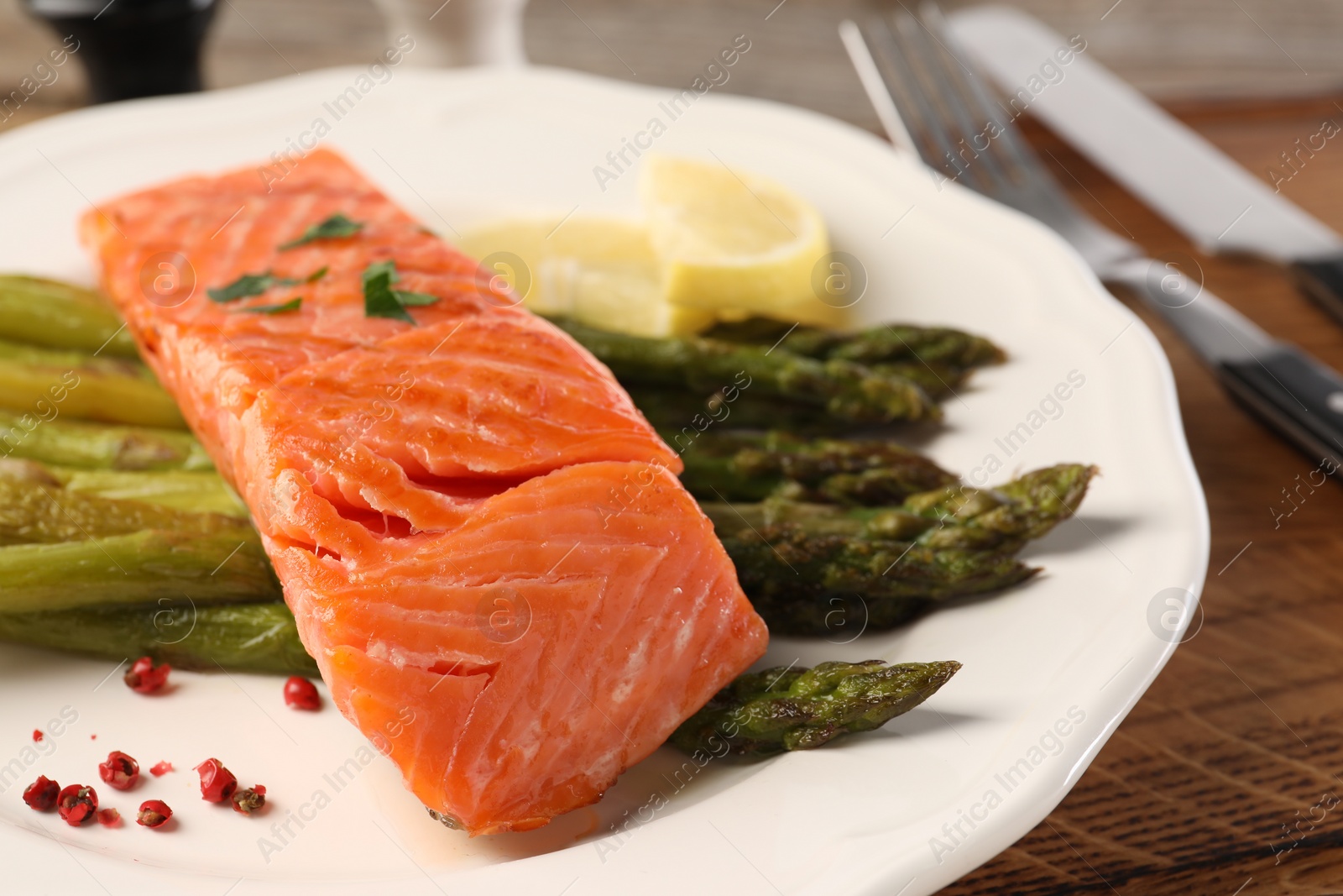 Photo of Tasty grilled salmon served with asparagus and lemon on wooden table, closeup