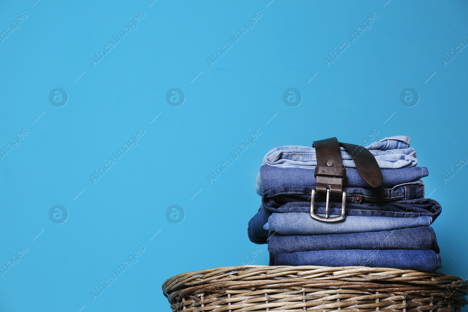 Photo of Stack of different jeans on basket against color wall with space for text