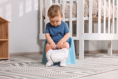 Little child sitting on plastic baby potty indoors
