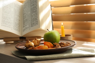 Dried fruits, apple, Bible and candle on window sill indoors. Great Lent season