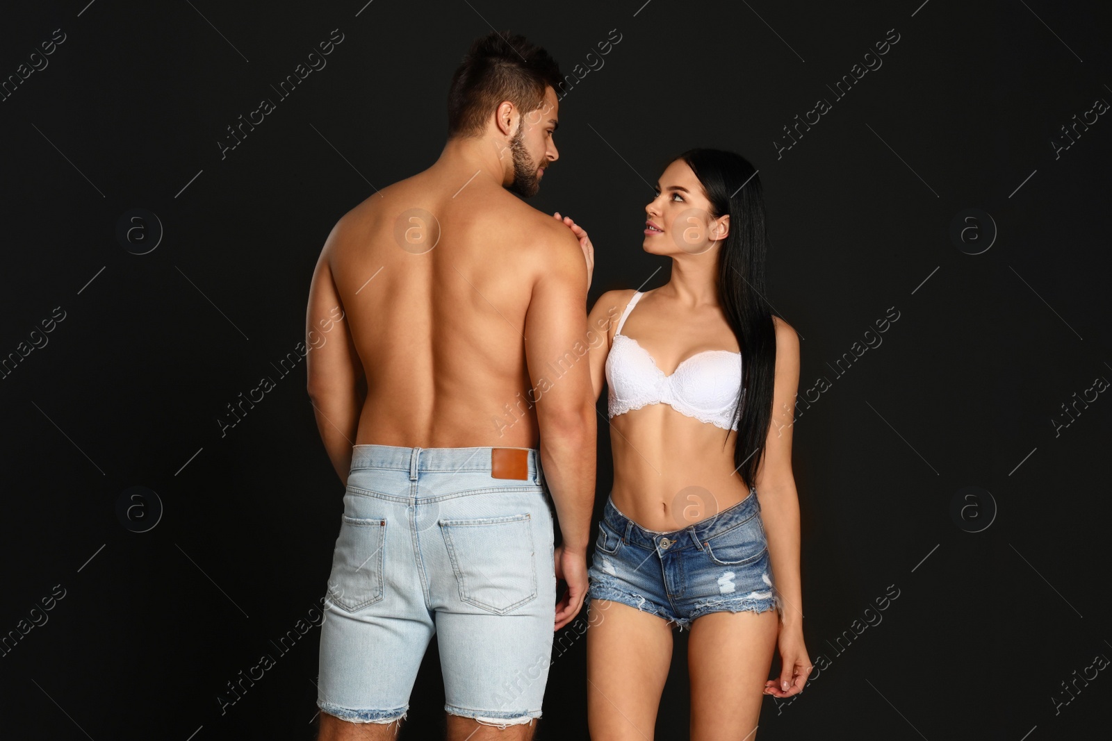 Photo of Young woman in underwear and denim shorts with her boyfriend on black background