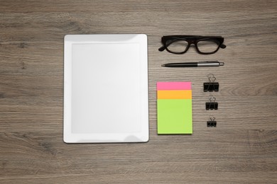 Photo of Modern tablet, glasses and office stationery on wooden table, flat lay. Distance learning