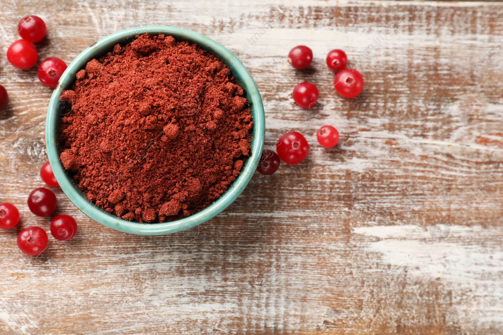 Photo of Cranberry powder in bowl and fresh berries on wooden table, top view. Space for text