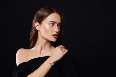 Young woman wearing elegant pearl bracelet on black background, space for text