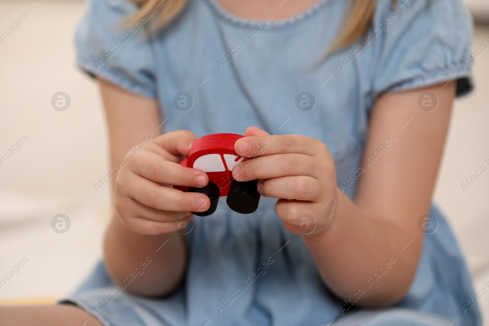 Photo of Little girl playing with wooden car on light background, closeup. Child's toy