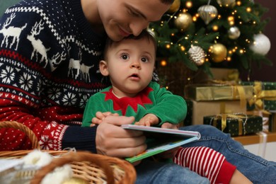 Father reading book to his cute son in room decorated for Christmas