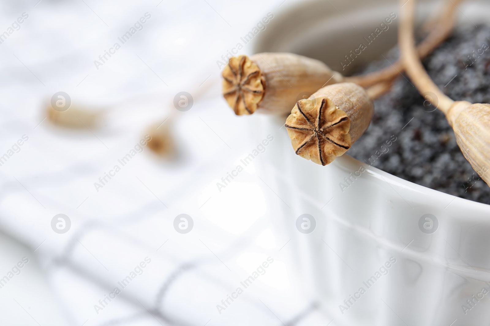 Photo of Bowl with dry poppy heads and seeds on table, closeup