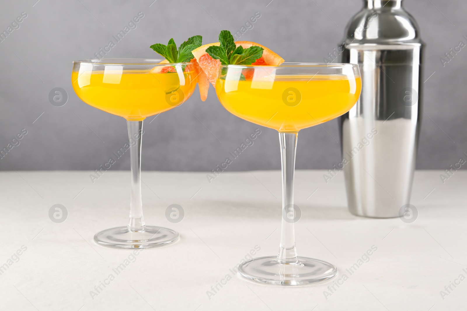 Photo of Delicious cocktail in glasses and metal shaker on light table