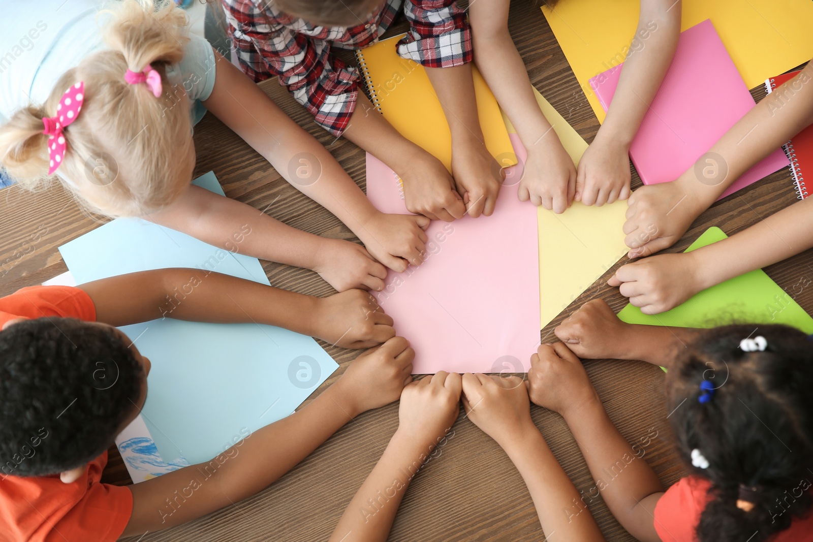 Photo of Little children putting their hands together at table, top view. Unity concept