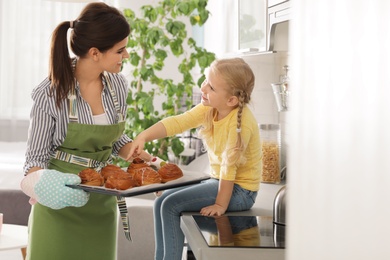 Daughter and beautiful mother with tray of oven baked buns in kitchen