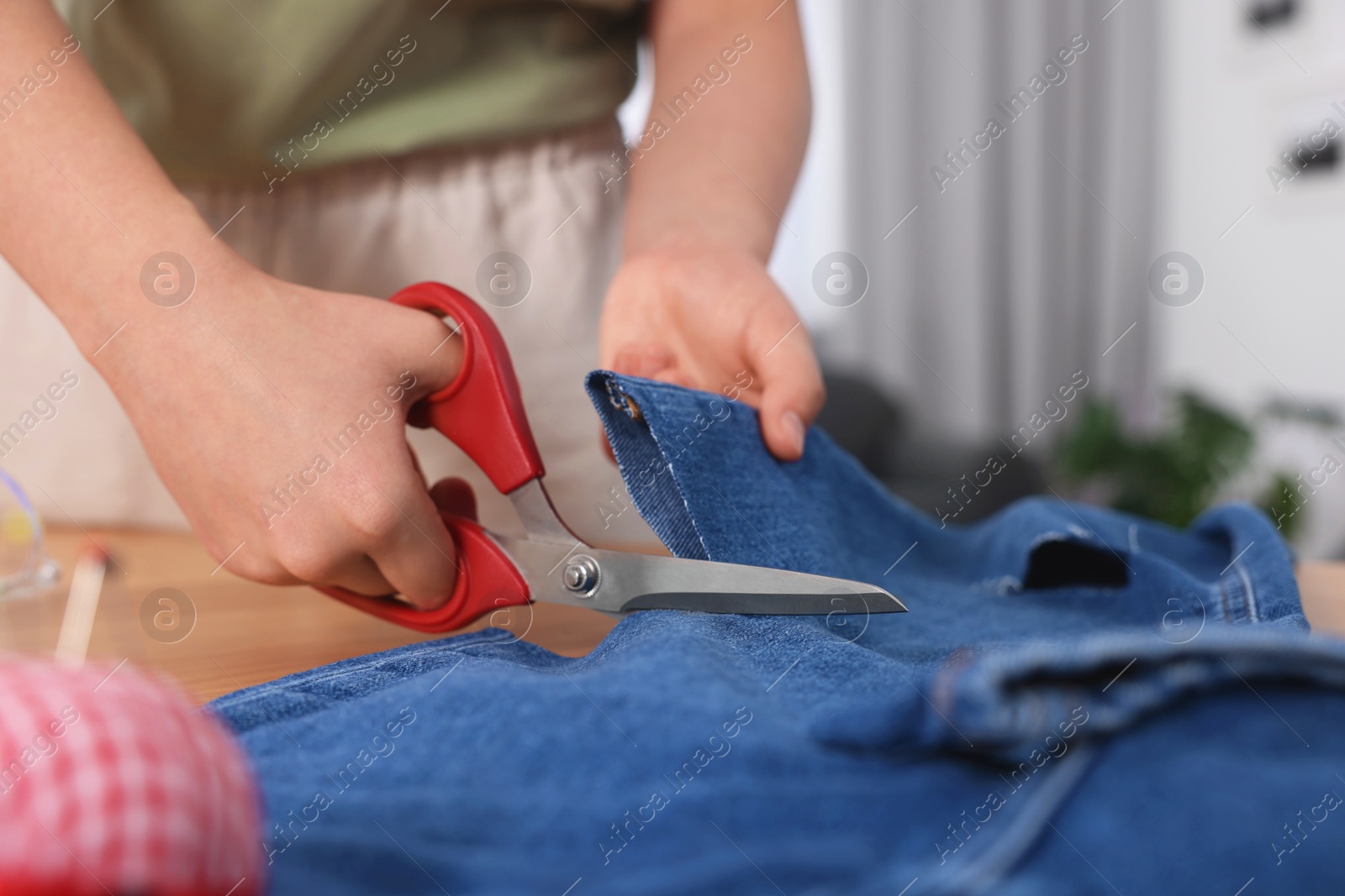 Photo of Woman cutting jeans with scissors at table, closeup