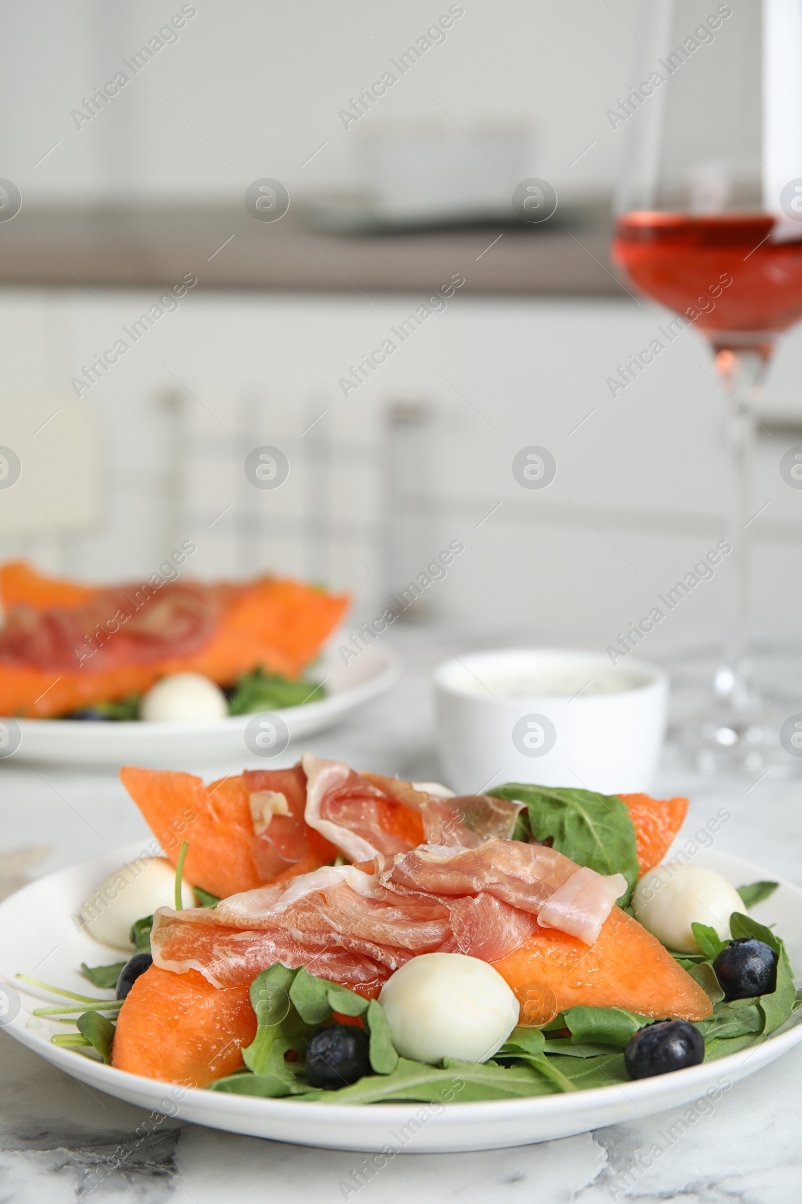 Photo of Fresh melon with prosciutto, mozzarella and arugula on marble table