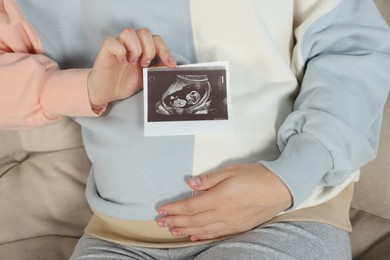 Photo of Pregnant woman with ultrasound picture of baby on sofa, closeup