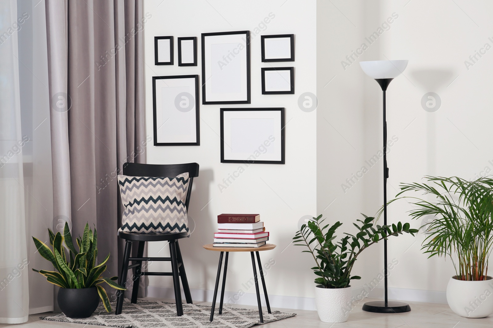 Photo of Empty frames hanging on white wall, wooden chair and table with books indoors