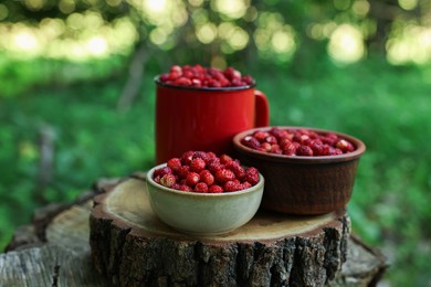 Dishes with tasty wild strawberries on stump against blurred background, closeup