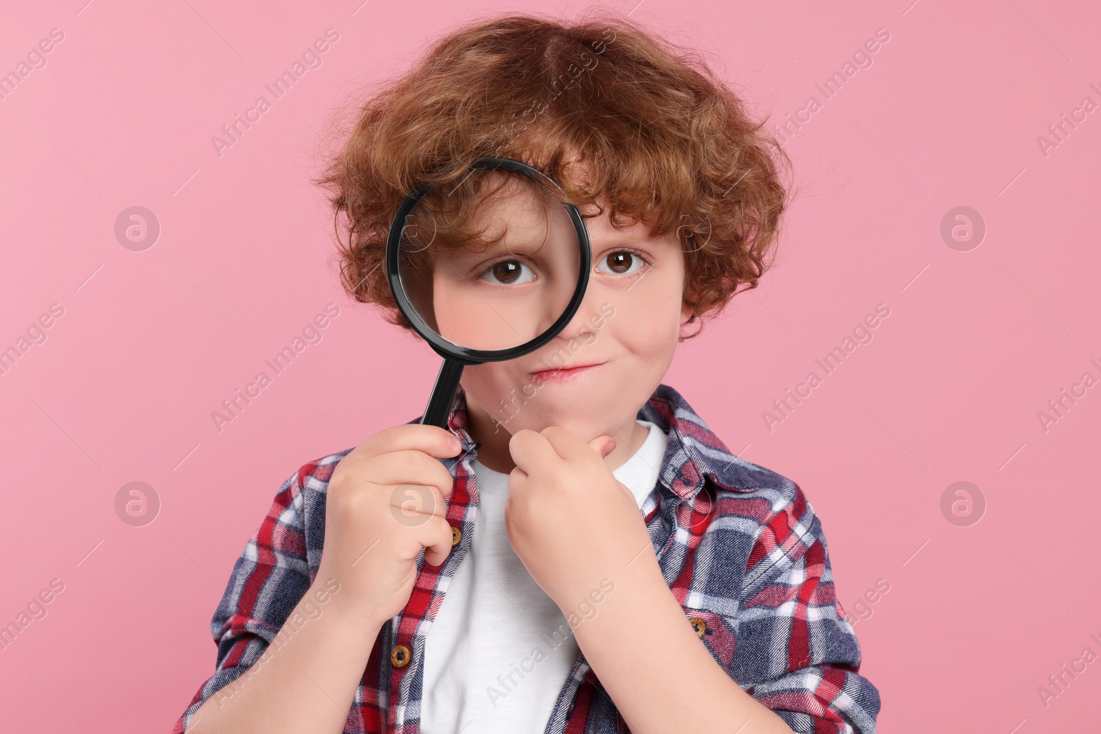 Photo of Cute little boy looking through magnifier glass on pink background