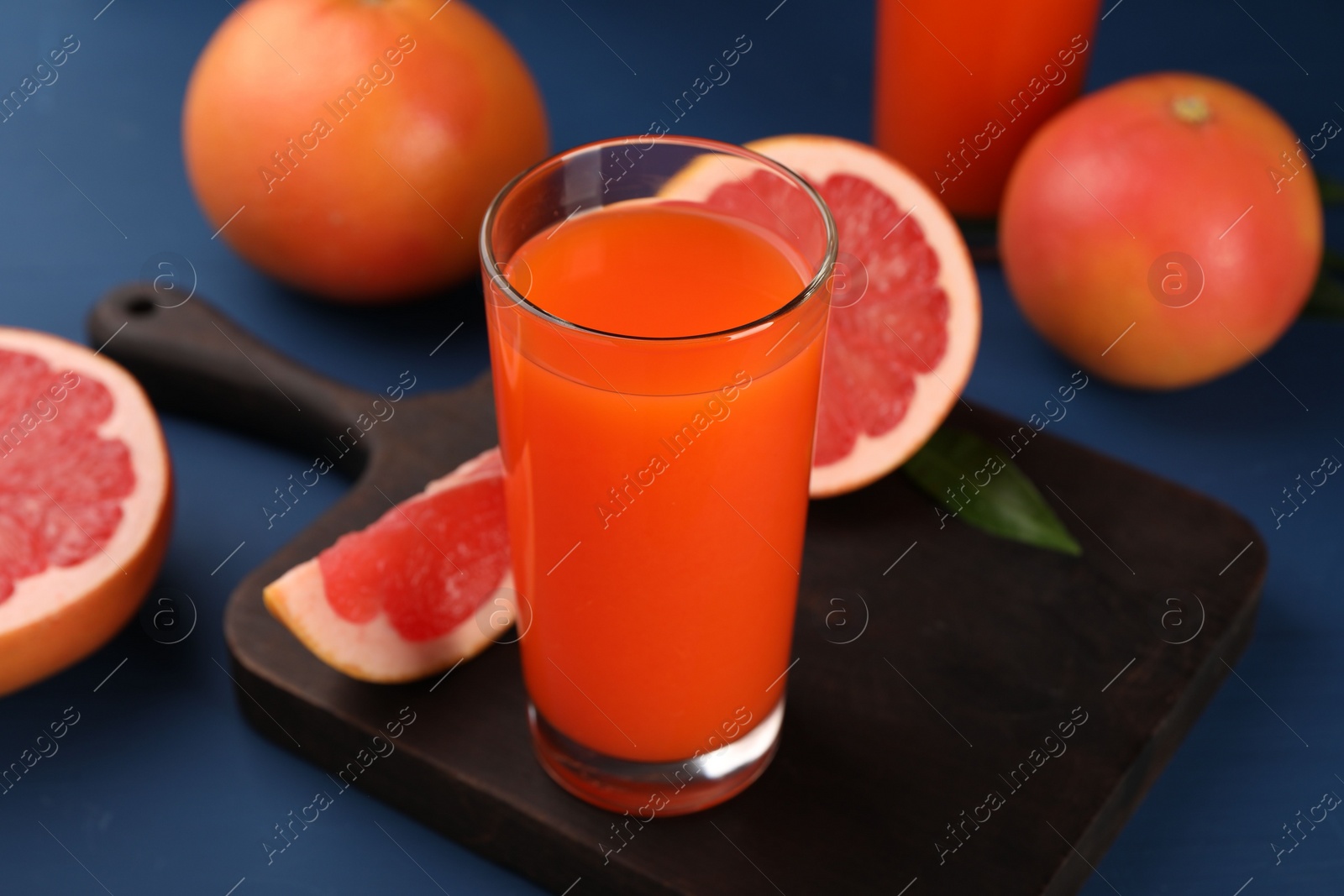 Photo of Tasty grapefruit juice in glass and fresh fruits on blue table, closeup