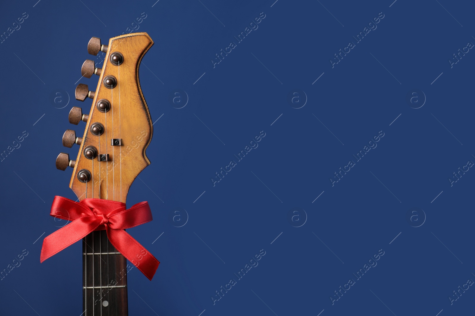 Photo of Guitar with red bow on blue background, space for text. Christmas music concept