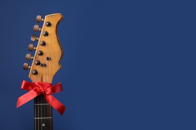 Guitar with red bow on blue background, space for text. Christmas music concept