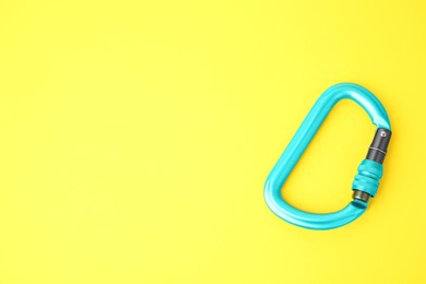 Photo of One light blue carabiner on yellow background, top view. Space for text