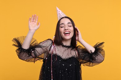 Photo of Happy woman in party hat with streamers on orange background